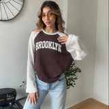 Woman wearing a brown and white raglan Brooklyn sweatshirt with light wash jeans