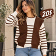 Woman in a cream and brown striped sweater with an attached brown vest layer and blue jeans outside a stone building
