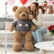 Caramel curly teddy bear in a grey knitted sweater with a bear face on the chest