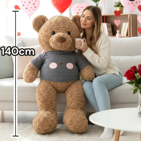 Caramel curly teddy bear in a grey knitted sweater with a bear face on the chest