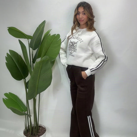 Side view of brown wide leg pants with white side stripes worn with a white varsity sweatshirt