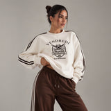 Close up of a white varsity print sweatshirt with brown sleeve stripes and brown drawstring pants