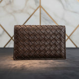 Brown woven leather wallet on a dark surface with a geometric patterned wall in the background