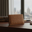 Brown woven leather wallet on a desk with a city view