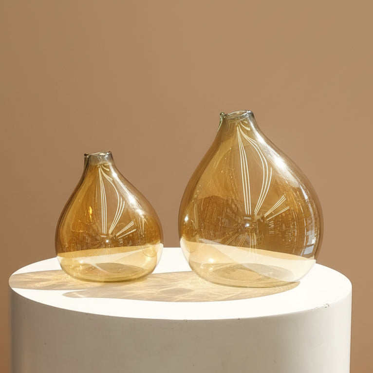 Both amber bubble vases standing empty side by side on a pale studio plinth