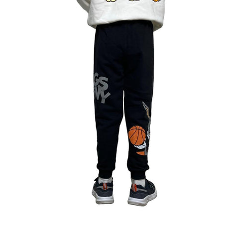 Child standing sideways in black joggers with large grey cartoon lettering across the thigh