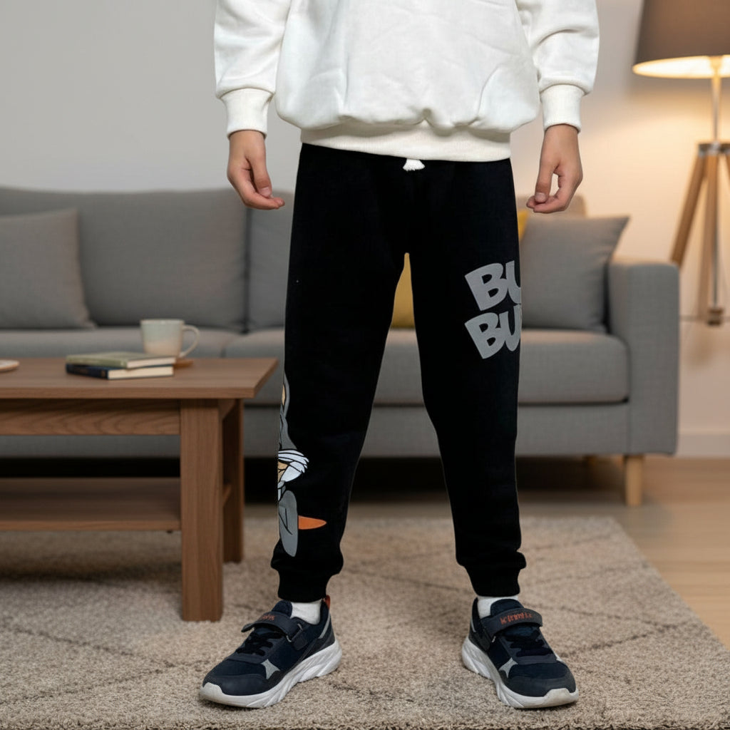 Boy wearing black cartoon rabbit joggers with grey lettering standing in a living room