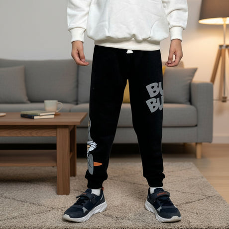 Boy wearing black cartoon rabbit joggers with grey lettering standing in a living room