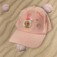Pink girls cap on rippled sand showing a rubber bunny patch with a gold dome centre