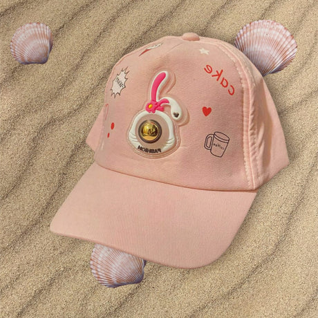 Pink girls cap on rippled sand showing a rubber bunny patch with a gold dome centre
