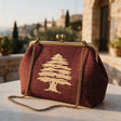 Burgundy frame clutch with a gold embroidered cedar tree, cypress trees and stone buildings behind