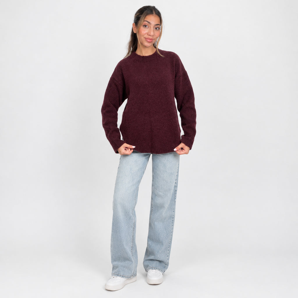 Full length view of an oversized burgundy knit sweater worn with wide leg jeans and sneakers