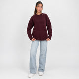 Full length view of an oversized burgundy knit sweater worn with wide leg jeans and sneakers