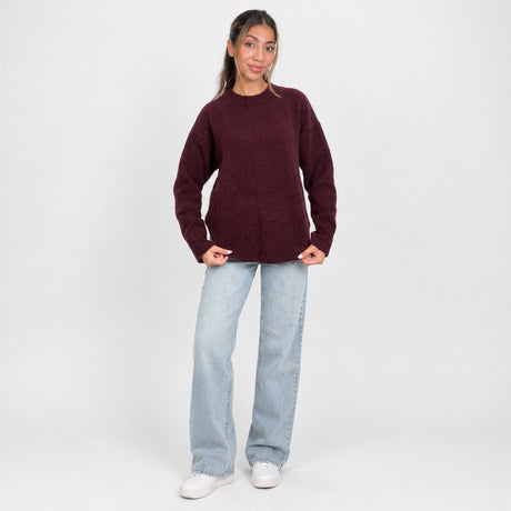 Full length view of an oversized burgundy knit sweater worn with wide leg jeans and sneakers