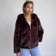 Burgundy faux fur hooded jacket with a glossy pile and gold zip worn over a white top
