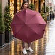 Woman on a wet street holding open a burgundy herringbone folding umbrella