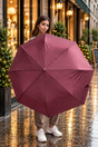 Woman on a wet street holding open a burgundy herringbone folding umbrella