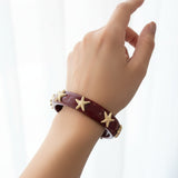 Hand wearing a burgundy bracelet with starfish charms on a white background