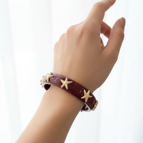 Hand wearing a burgundy bracelet with starfish charms on a white background