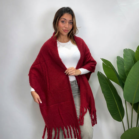 Woman wearing a burgundy brushed blanket scarf draped open over a white top with tassel ends