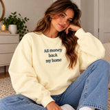 Woman in a butter yellow sweatshirt with an All Money Back My Home slogan print and light blue jeans