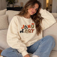 Woman in a butter yellow crew neck sweatshirt with colourful January lettering and a puppy print, sitting in jeans