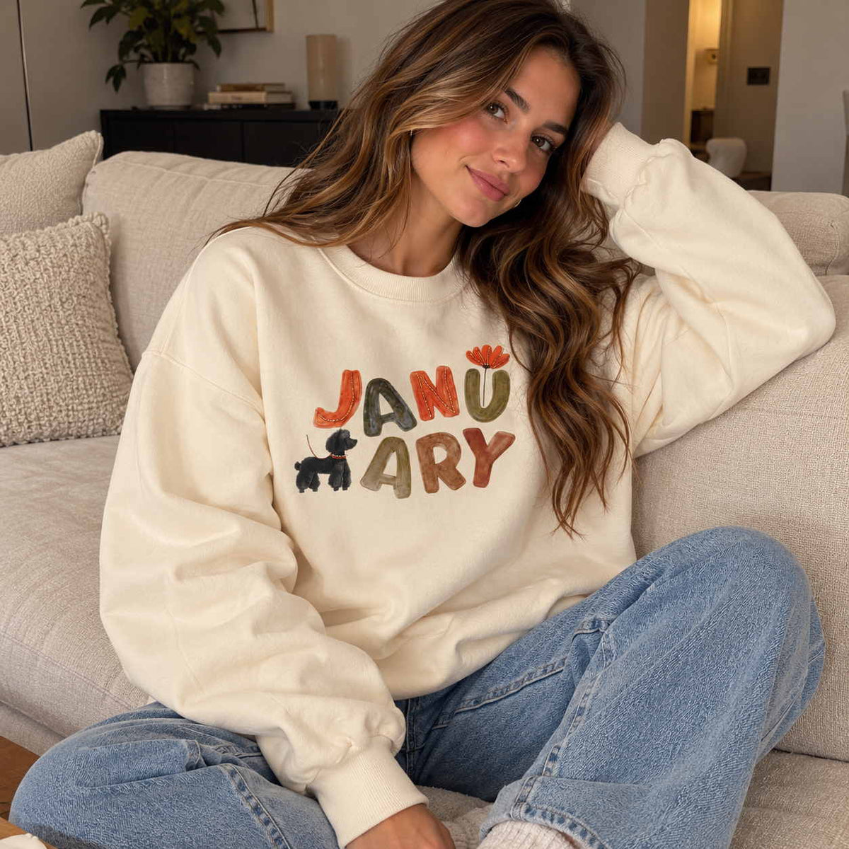 Woman in a butter yellow crew neck sweatshirt with colourful January lettering and a puppy print, sitting in jeans