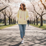 Butter yellow zip hoodie worn zipped with hands in the side pockets on a park path