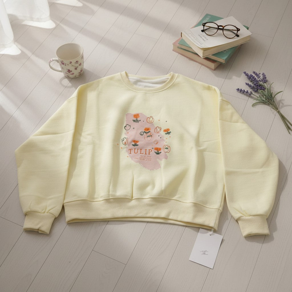 Butter yellow tulip print sweatshirt laid flat beside books and lavender