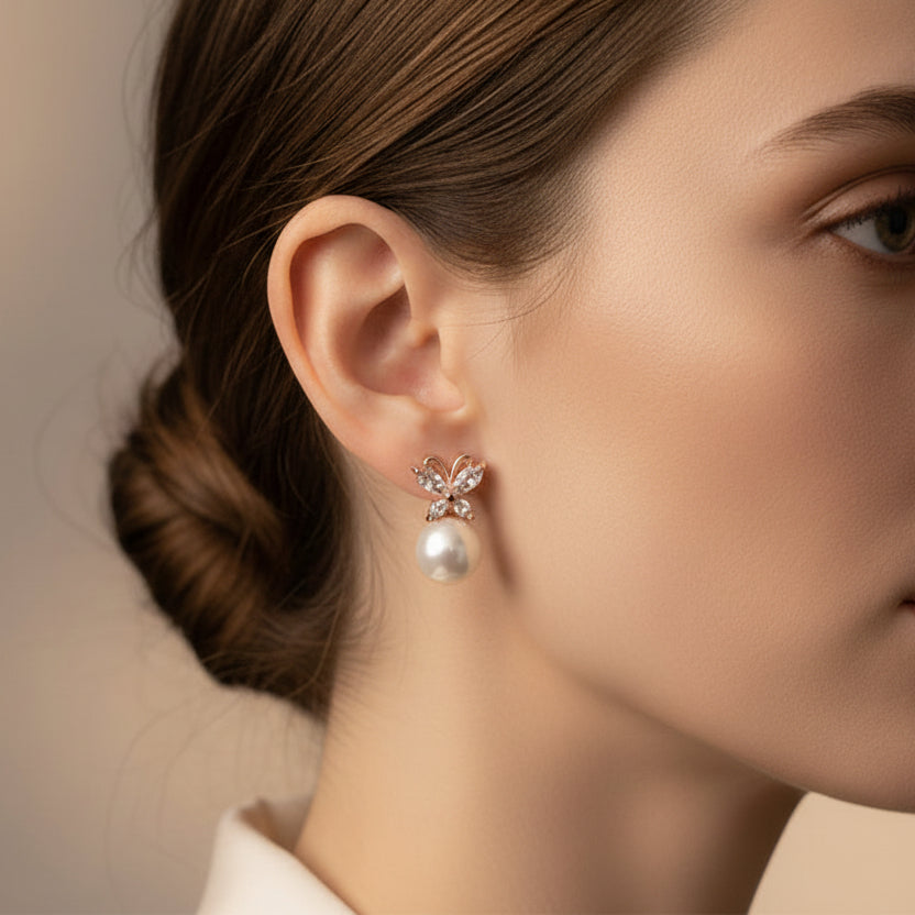 Close-up of a woman wearing butterfly pearl earrings with a neutral background