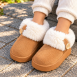 Child wearing camel faux suede slipper boots with a fluffy white cuff and wooden buttons
