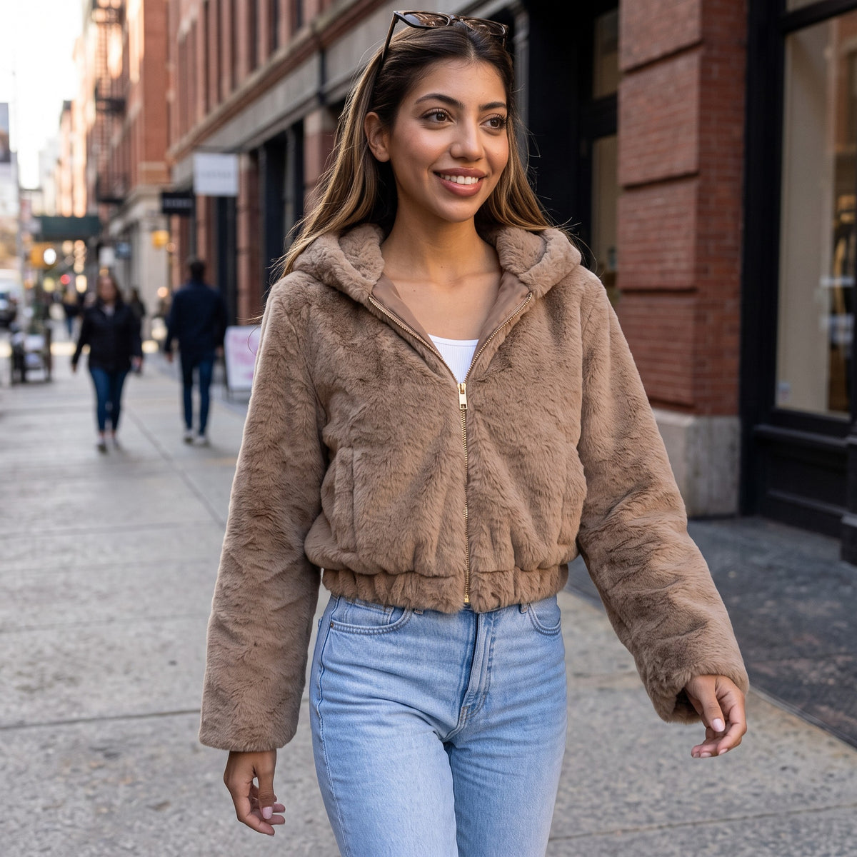 Woman walking a city street in a short camel faux fur hooded jacket zipped up