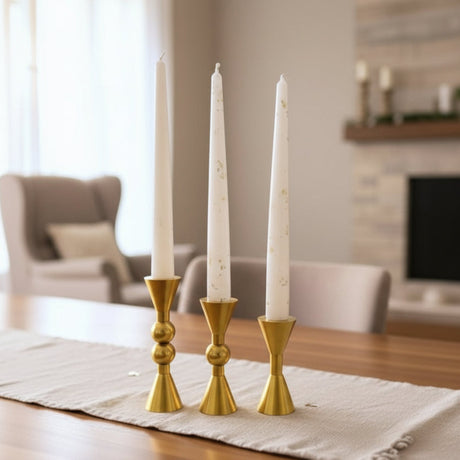 The three squat gold holders on a fringed runner before a white stone fireplace