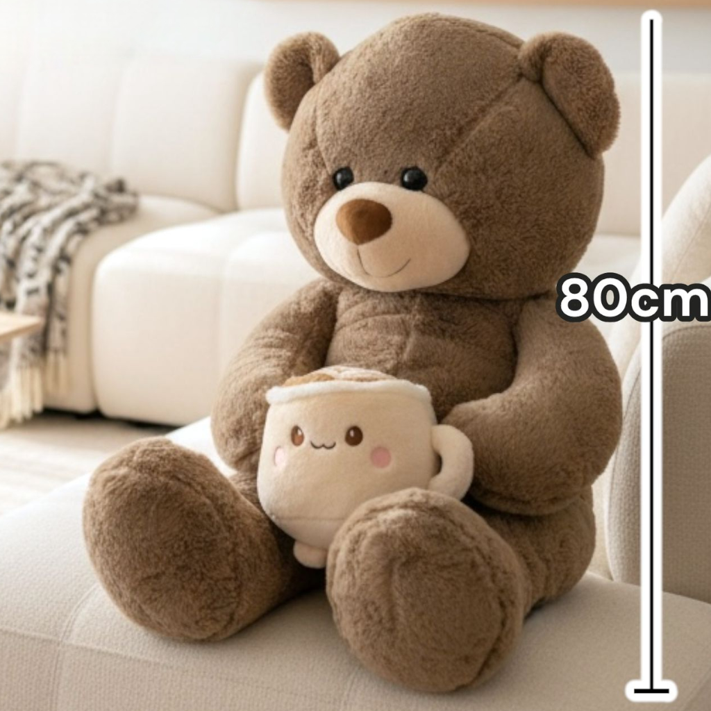 Seated mocha bear on a white sofa, the grinning latte mug plush resting between its paws