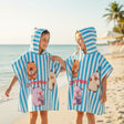 Two children on the beach wearing blue and white striped capybara poncho towels