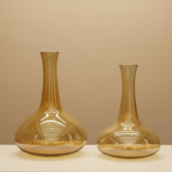 Two empty amber carafes with flared bases and long slender necks on a beige backdrop