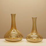 Two empty amber carafes with flared bases and long slender necks on a beige backdrop