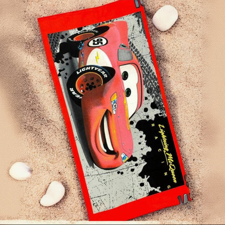 Lightning McQueen racing print beach towel with a red border laid on pale sand