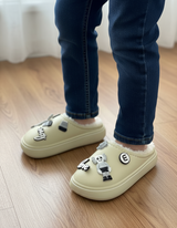 Cream slippers with charm details worn with jeans on a wooden floor