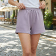 Person wearing light purple shorts and a white top outdoors on a sunny day.