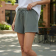 Person wearing green shorts and a white top outdoors on a sunny day.