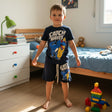 Boys navy two piece set with a surf dinosaur print tee and matching shorts, worn in a bedroom