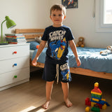 Boys navy two piece set with a surf dinosaur print tee and matching shorts, worn in a bedroom