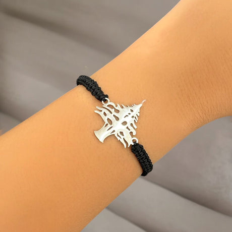Bracelet with a silver cedar charm on a wrist against a neutral background