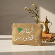 Jute zip pouch stitched in white with a two line Arabic phrase and a green cedar tree