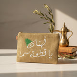 Jute zip pouch stitched in white with a two line Arabic phrase and a green cedar tree
