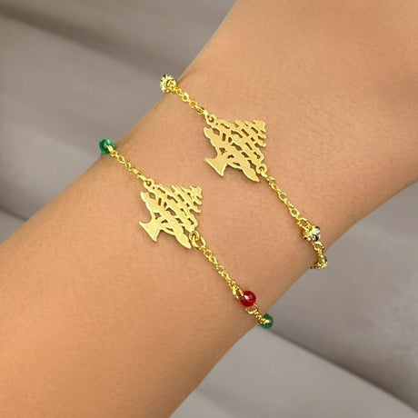 Gold bracelet with cedar tree charms on a wrist against a neutral background