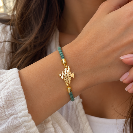 Green braided cord bracelet with a gold cedar tree charm and gold end caps on a wrist