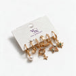 Six single gold huggie earrings with pearl, star, rainbow planet and starburst charms on a white card