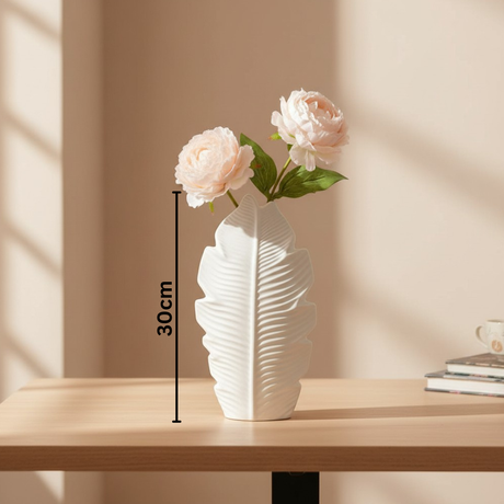 A rounder leaf vase holding two cream peonies under striped window shadow, marked 30cm